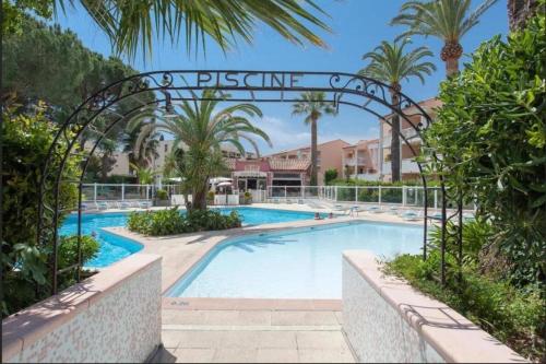 einen Pool in einem Resort mit einem Torbogen und Palmen in der Unterkunft Appartement cosy vue mer, 5min à pied de la plage, parking in Vallauris