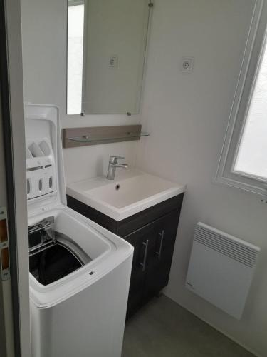 une petite salle de bains blanche avec lavabo et lave-linge. dans l'établissement Mobilhome Luminosa tt équipé 6/8 pers, aux Mathes