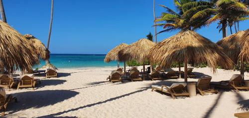 - une plage avec des chaises et des parasols en paille et l'océan dans l'établissement Private Villa LaPerla Iberosta 3BDR, Pool, Beach, WiFi, à Punta Cana