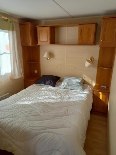 um quarto com uma grande cama branca e armários de madeira em mobilhome nature em Saint-Laurent-sur-Mer