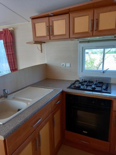 a small kitchen with a stove and a sink at mobilhome nature in Saint-Laurent-sur-Mer