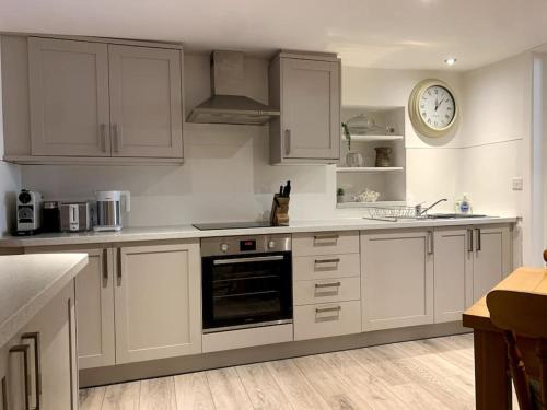 uma cozinha com armários brancos e um relógio na parede em The Vottage - 3 bed cottage em Plymouth