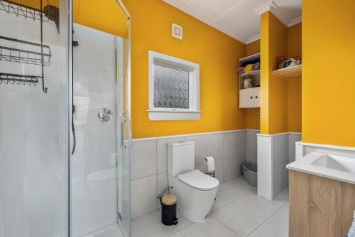 a bathroom with a toilet and a shower and yellow walls at The Chapel- Kohukohu in Kohukohu Town District