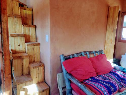 a bedroom with a bed with red pillows and wooden shelves at Cabaña Misk'i Nuna, en las afueras de Tilcara in Tilcara