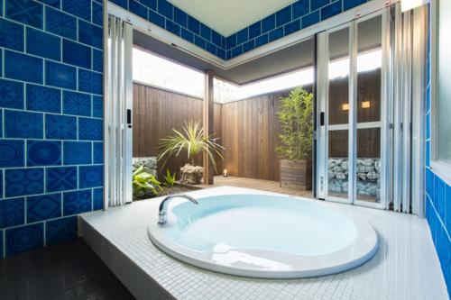 a tub in a bathroom with blue tiles at Ufufu Village in Izu