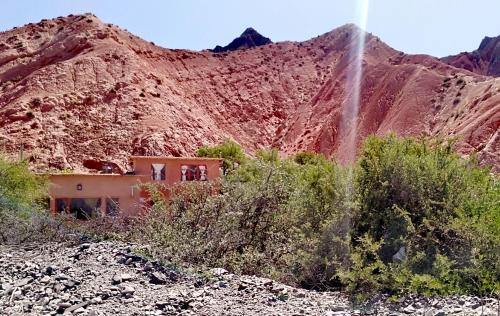 a house in front of a mountain with a waterfall at Cabaña Misk'i Nuna, en las afueras de Tilcara in Tilcara