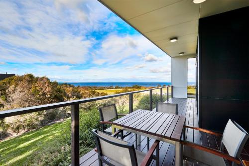 einen Balkon mit einem Holztisch, Stühlen und Meerblick in der Unterkunft RACV Inverloch Resort in Inverloch