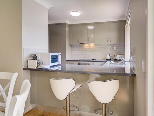 a kitchen with two white chairs and a counter at Breeze in Toogoom in Toogoom