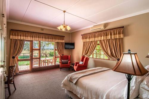 een hotelkamer met een bed, een stoel en ramen bij Mooiplaas Guesthouse in Oudtshoorn