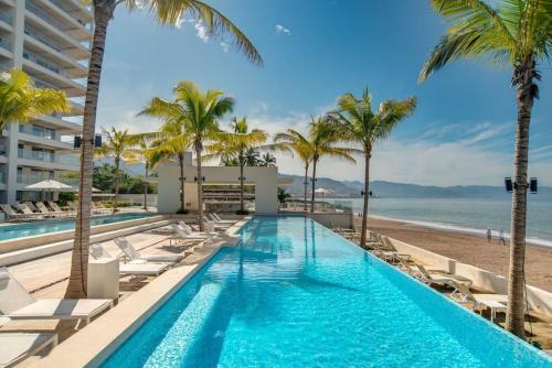 a swimming pool with chairs and palm trees on the beach at Harbor 9005 Beachfront 2bdr by Moikkarentals in Puerto Vallarta