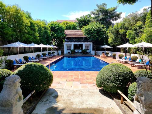 a swimming pool in a yard with chairs and umbrellas at Rachamankha Hotel in Chiang Mai