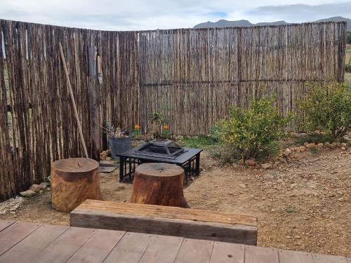 a patio with a table and two logs and a fence at Pom Gratz - EcoDomes in Hartebeest Rivier
