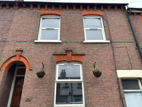 a brick building with three windows with flower baskets at Luton Town House Near AIRPORT in Luton