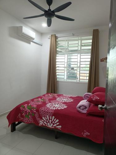 - une chambre avec un lit doté d'une couverture rouge et d'un ventilateur dans l'établissement Yasmeen Homestay Kijal Nenas 2, à Kijal