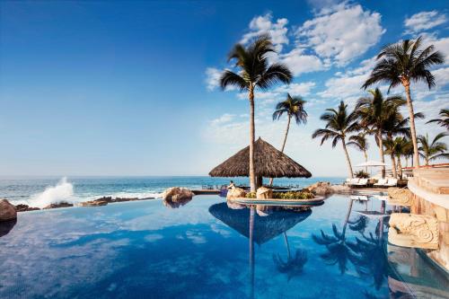 a pool at a resort with palm trees and the ocean at One&Only Palmilla in San José del Cabo