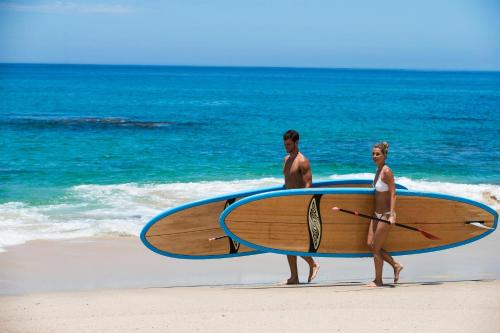 a man and woman walking on the beach with a surfboard at One&Only Palmilla in San José del Cabo