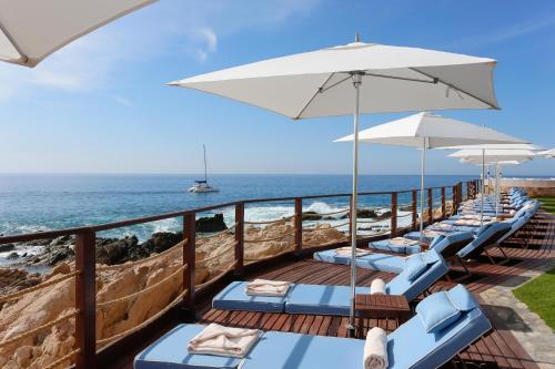a row of lounge chairs with umbrellas and the ocean at One&Only Palmilla in San José del Cabo