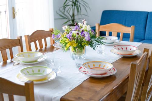 a wooden table with plates and bowls and flowers on it at SorrentoVibes - Sea view Rooftop Apartment with Jacuzzi & Garden in Sorrento