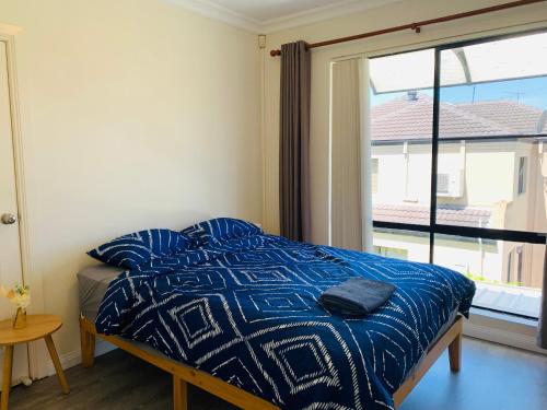 a bedroom with a bed with a blue comforter and a window at Comfy place with all in Revesby