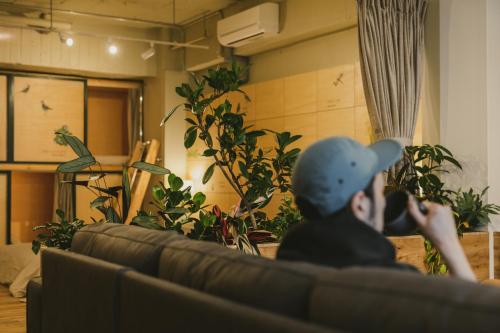 Ein Mann, der auf einer Couch in einem Zimmer mit Pflanzen sitzt. in der Unterkunft DENCHI TOKYO - Guest House DENCHI in Tokio