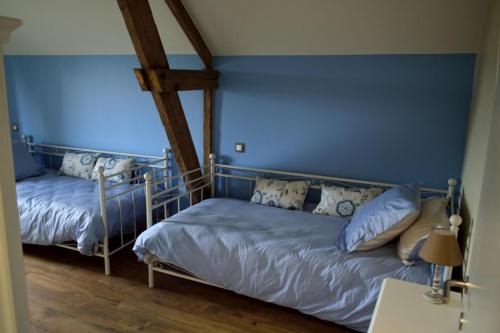 two beds in a room with blue walls and wooden floors at La grange des deux pays in Nieppe