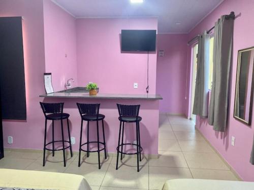 uma cozinha com paredes cor-de-rosa e bancos de bar em Pousada Mercosul em Alegrete