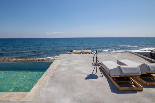 a swimming pool with two lounge chairs and the ocean at Casa di Mare Luxury Villas in Imerovigli