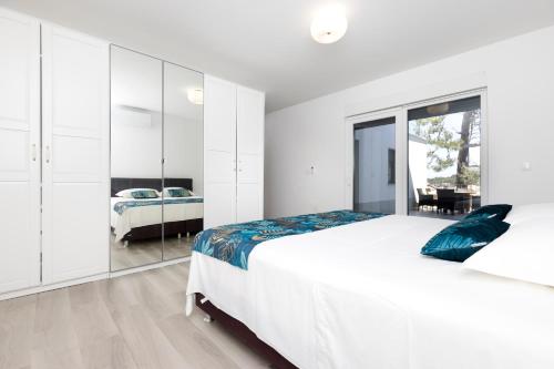 a white bedroom with a large bed and a mirror at Apartments Olea in Mali Lošinj