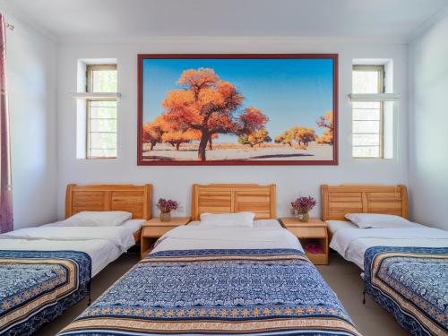 une chambre avec trois lits et un tableau mural dans l'établissement Dunhuang Hu Yang Inn, à Dunhuang