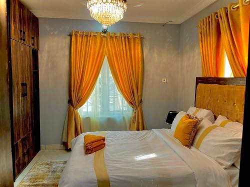 1 dormitorio con 1 cama con cortinas de color naranja y lámpara de araña en The Moonshine Residence-Royal, en Nnewi