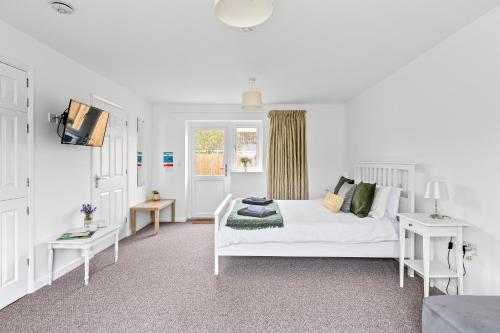 a white bedroom with a white bed and a tv at Number 7 - Lytton Tree Lodge, Reydon, Southwold in Reydon