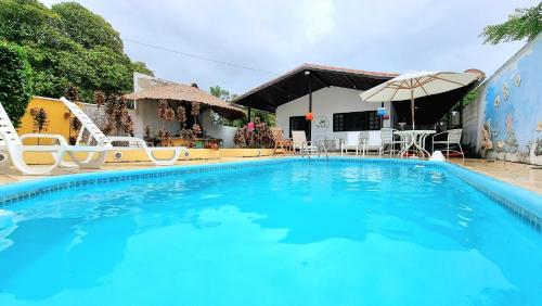 a large swimming pool with chairs and an umbrella at Pousada Flor de Lótus Suites Carneiros in Tamandaré