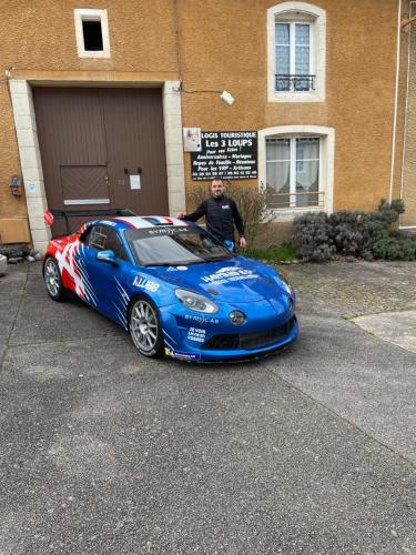 a man is standing next to a blue car at Logîte Touristique Les 3 Loups in Châtenois
