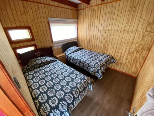 two beds in a small room with wooden walls at Cabaña casa 6 personas, con vista al mar in Dalcahue