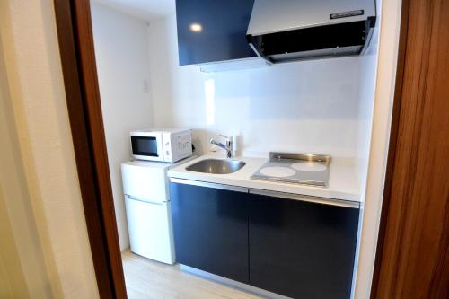 eine kleine Küche mit einer Spüle und einer Mikrowelle in der Unterkunft オリエントシティ南堀江Ⅱ in Osaka