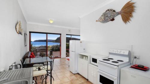 a kitchen with white appliances and a dining room with a table at Beachcomber - Waterfront Umina Beach Wifi in Umina