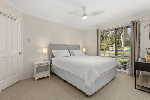 a white bedroom with a bed and a window at Crowford Sands by Experience Jervis Bay in Sanctuary Point