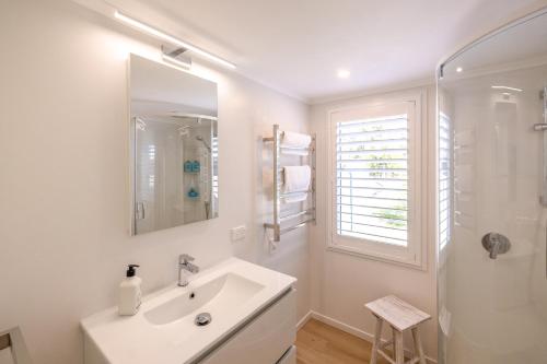 a white bathroom with a sink and a shower at Bach on the Beach - Coast & Country in Onetangi
