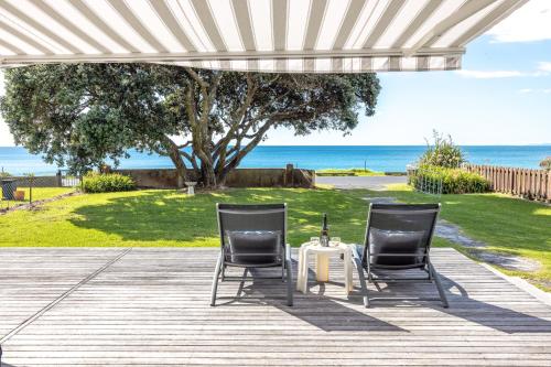 two chairs and a table on a deck with the ocean at Bach on the Beach - Coast & Country in Onetangi