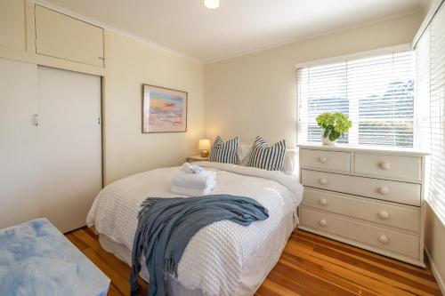 a bedroom with a bed and a dresser and a window at Bach on the Beach - Coast & Country in Onetangi