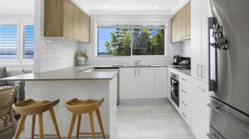a kitchen with white cabinets and a counter and stools at Sam's Shack Waterfront Woy Woy Bay in Woy Woy
