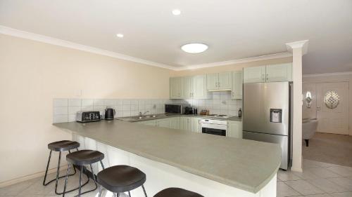 a kitchen with a large counter with stools and a refrigerator at Banksia Villa Umina Beach in Umina