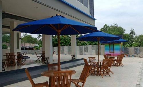 eine Gruppe von Tischen und Stühlen mit blauen Sonnenschirmen in der Unterkunft The Holiday Guest House in Tanjungpandan