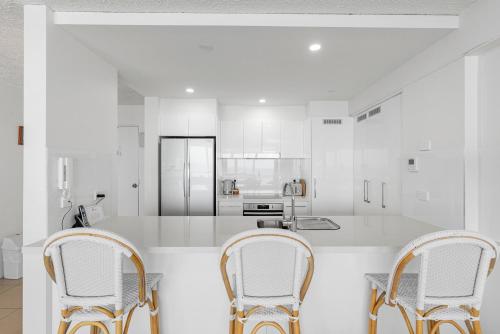 a white kitchen with two chairs and a counter at 84 The Spit Holiday Apartments in Mooloolaba
