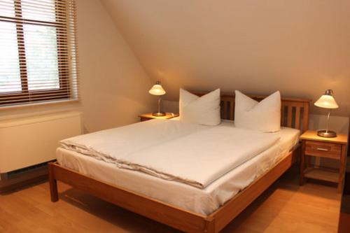 Ferienhäuser Ferienhaus Xenia في ويك: غرفة نوم بسرير مع شراشف بيضاء ومصباحين