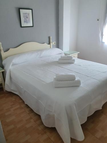 Una cama blanca con dos toallas encima. en Hostal Carlos III en Aldea Quintana