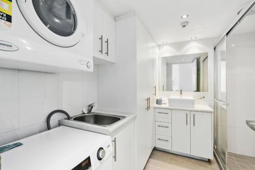 een witte badkamer met een wastafel en een wasmachine bij Cosmopolitan - Hosted by Coastal Letting in Gold Coast