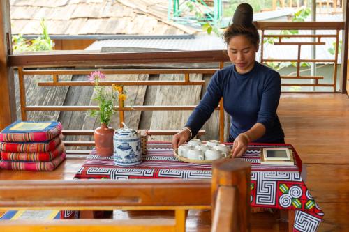 a woman standing next to a table with a plate of dishes at Truong Nhan Tram Tau Homestay in Cham Ta Lao
