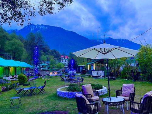 Himalayan Nature Walk Resort, Manali في مانالي: مجموعة من الكراسي والطاولات مع مظلة