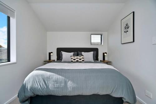a white bedroom with a large bed with two tables at Āta Haere - Christchurch Holiday Homes in Christchurch